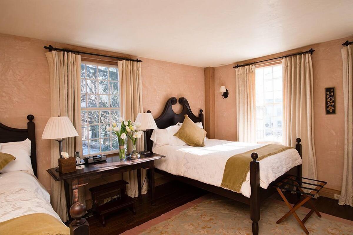 A bedroom with two single beds, a bedside table with lamps, a nightstand, and a window with curtains.