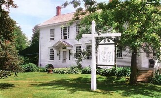 Una casa blanca de dos pisos con un letrero que dice "The Old Inn on the Green".