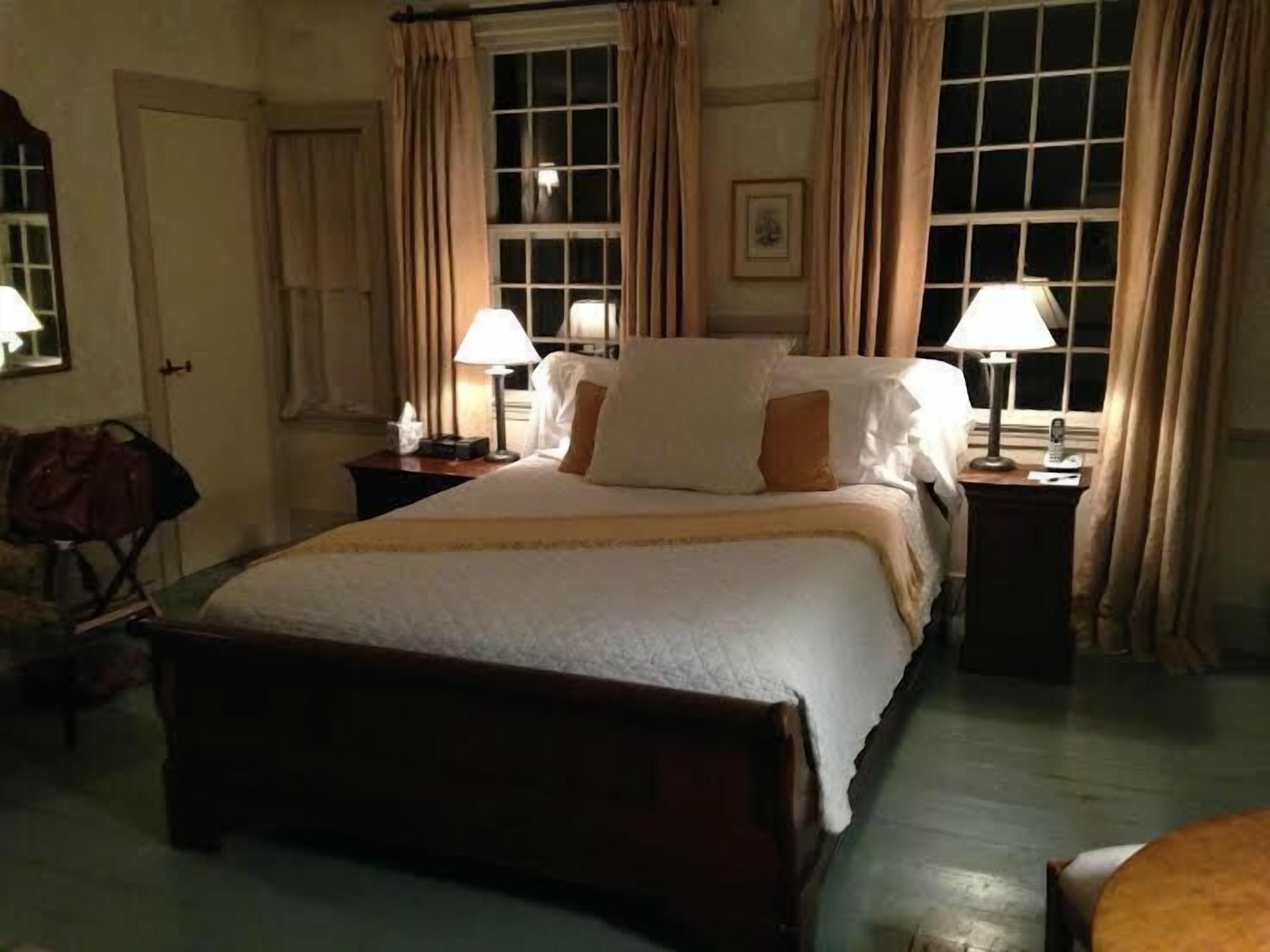 A hotel room with a large bed, two bedside tables with lamps, a wooden bench, and a window with curtains.