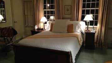 A hotel room with a large bed, two bedside tables with lamps, a wooden bench, and a window with curtains.