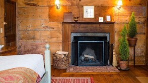 A cozy room with a fireplace, wooden walls, a bed with a patterned bedspread, and two wall-mounted lamps. - The Old Inn On The Green (Great Barrington)