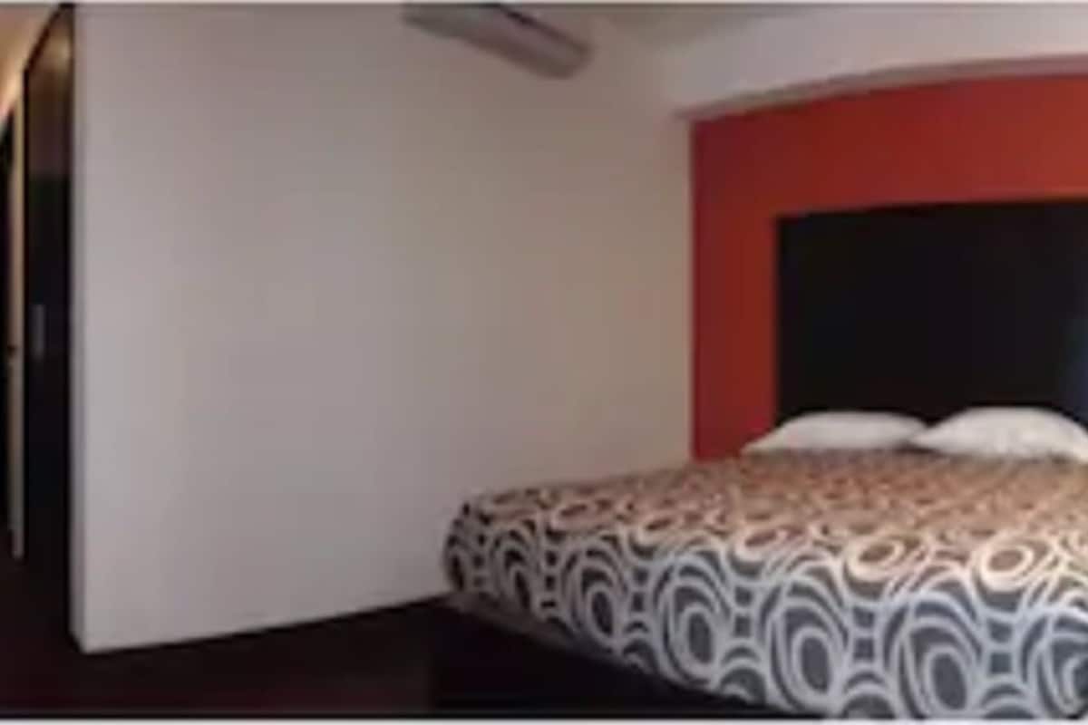 Une chambre d’hôtel avec deux lits, un mur d’accent rouge et une grande fenêtre avec des rideaux.