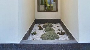 Een smalle, afgesloten buitenruimte met een groot raam en een kleine tuin aangelegd met witte kiezelstenen en enkele planten.