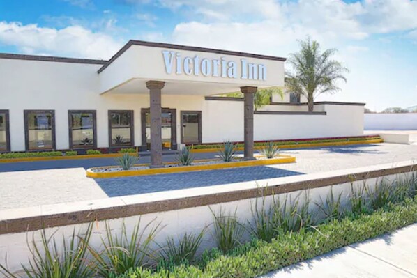 The exterior of Victoria Inn, featuring a modern design with a prominent entrance, columns, and a landscaped area with plants. - Hotel Victoria Inn (San Juan del Río)