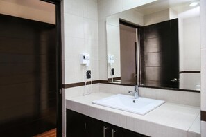 A modern bathroom with a white sink, a large mirror, and two hand dryers.