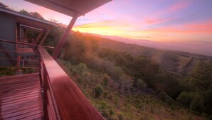 Ein Holzbalkon mit Blick auf ein bewaldetes Tal und Sonnenuntergang.