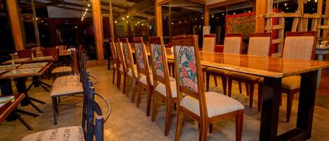 A restaurant with wooden tables and chairs, large windows, and a warm interior lighting.