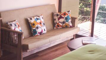 A wooden sofa with colorful circular-patterned cushions, a small table, and a view of greenery outside.