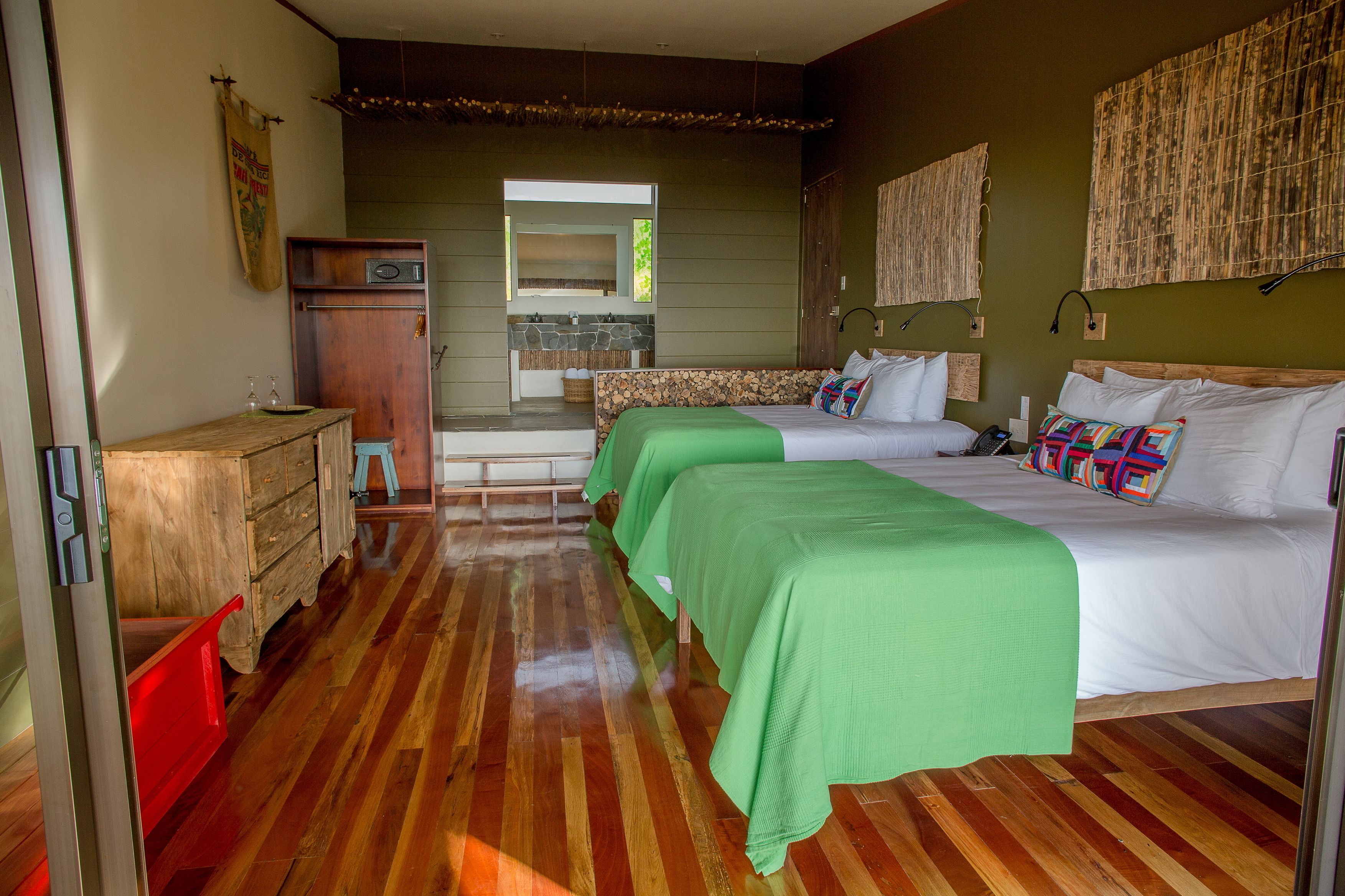 Een kamer met twee bedden, een houten dressoir, een kitchenette en een groot raam.