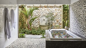 Un baño con pared de piedra, una bañera con flores y una pared cubierta de plantas.