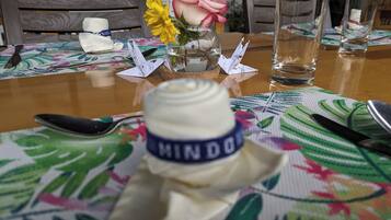 Une table recouverte d’une nappe à motifs floraux, une bouteille d’eau, un verre, une cuillère, un couteau et un porte-serviettes orné d’une rose.