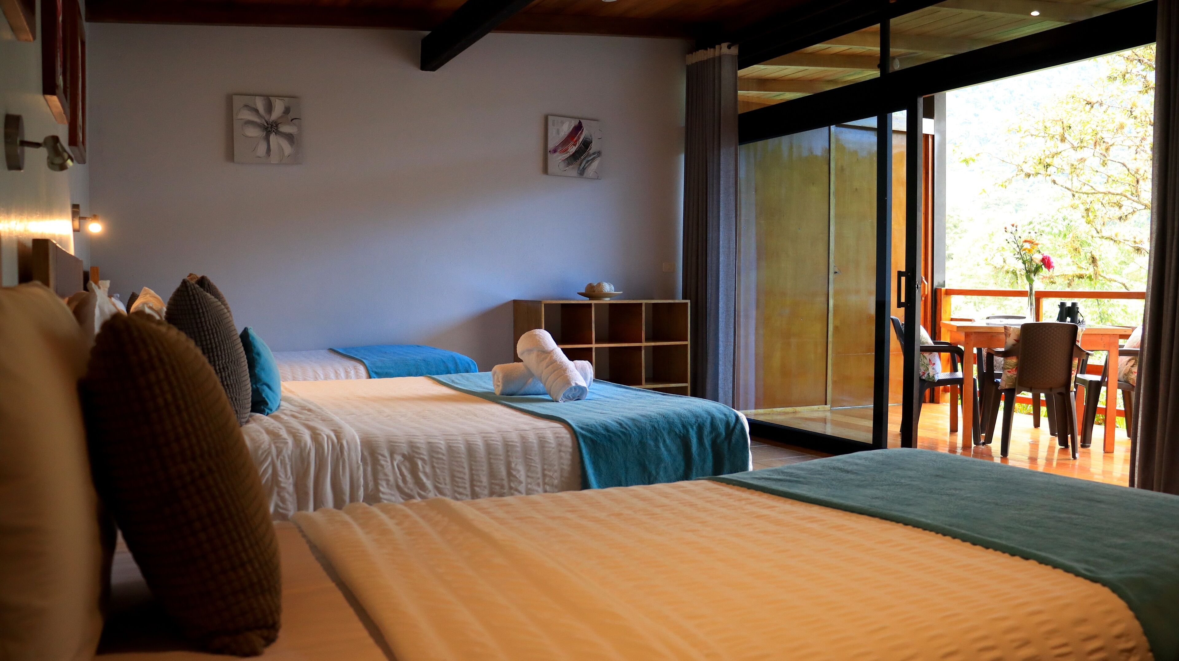 Habitación de hotel con dos camas, un armario de madera y un balcón con mesa y sillas.