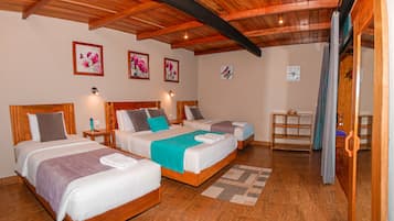 Habitación de hotel con tres camas, suelo de madera y techo con vigas a la vista.