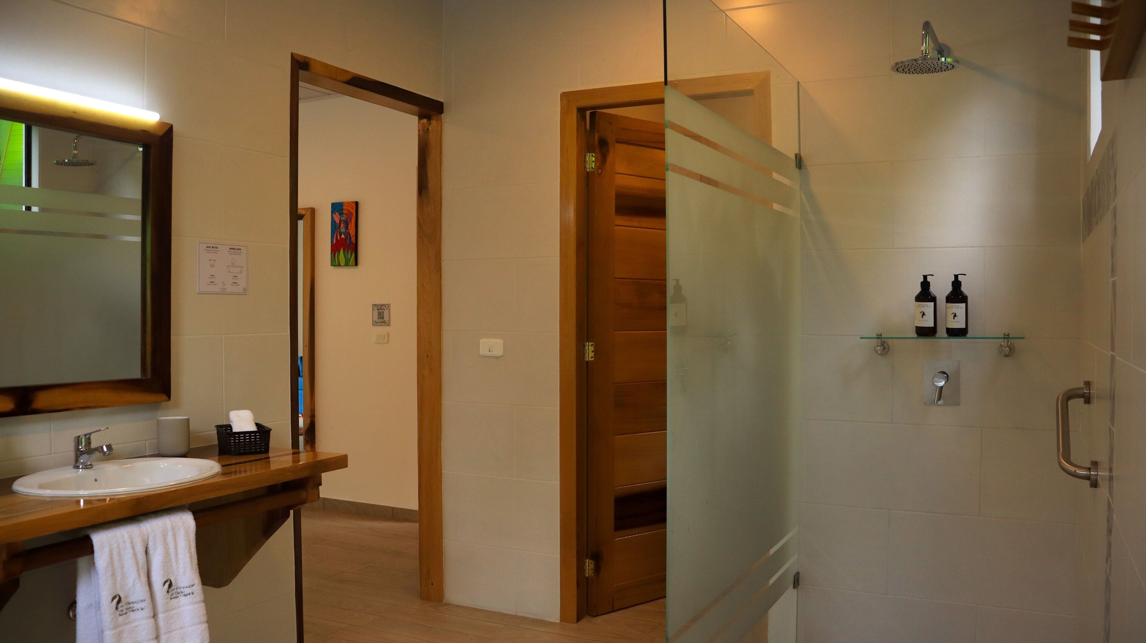 Un baño con tocador de madera, espejo, cabina de ducha de vidrio y repisa con artículos de aseo.