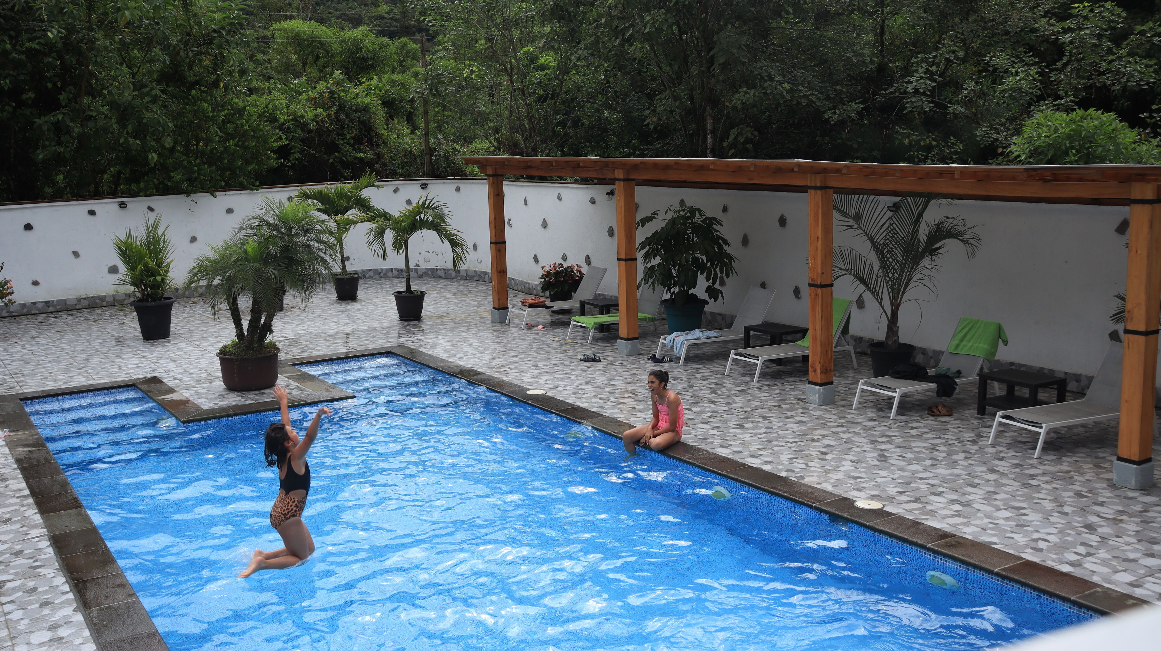 A swimming pool with a tiled deck, surrounded by lounge chairs and potted plants.