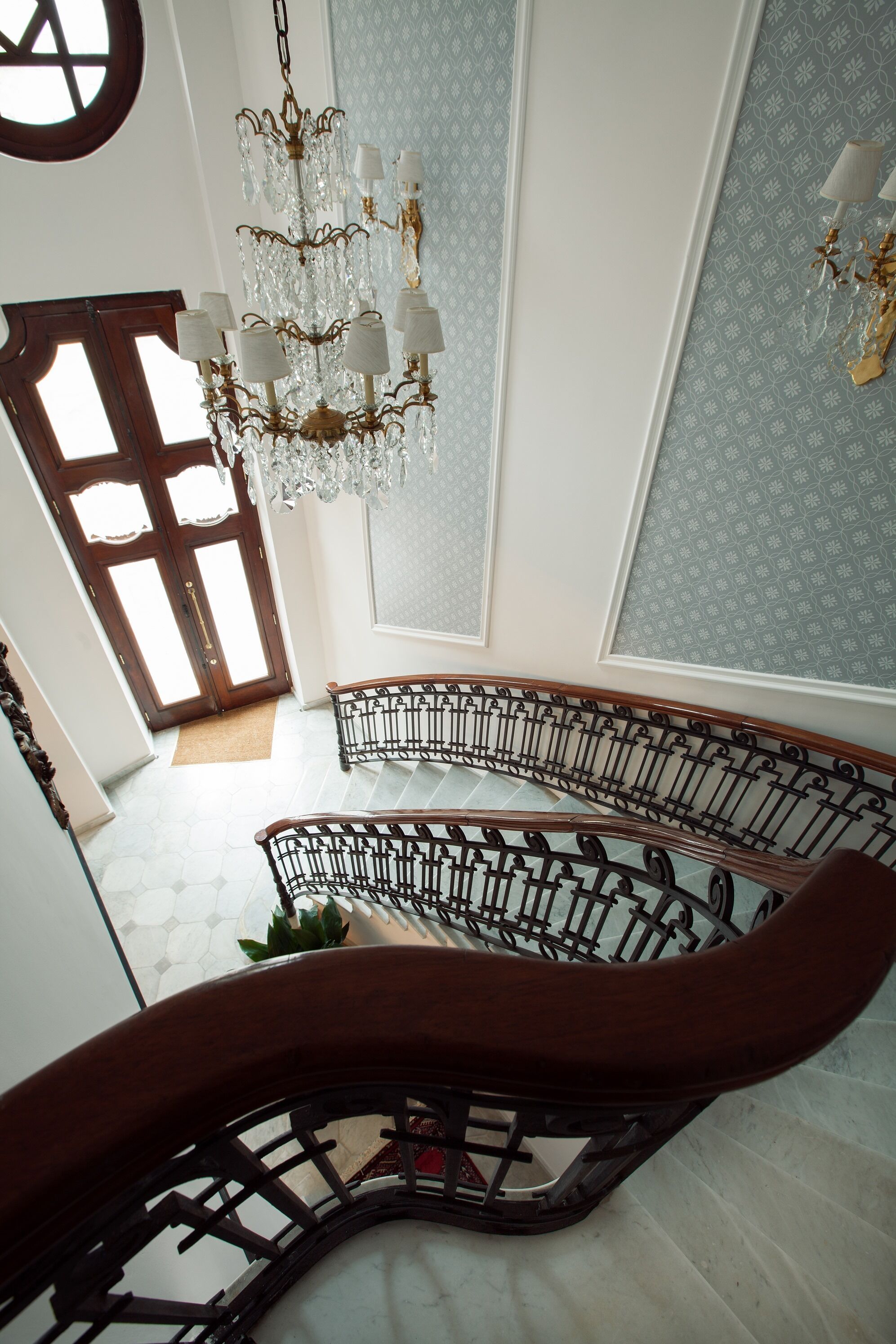 A grand staircase with a black metal railing, a chandelier, and a patterned wall.