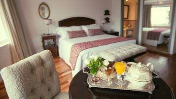 Une chambre d’hôtel avec un lit, une table de chevet, une chaise et un plateau sur lequel se trouvent une théière, un verre de jus d’orange et un vase avec des fleurs.