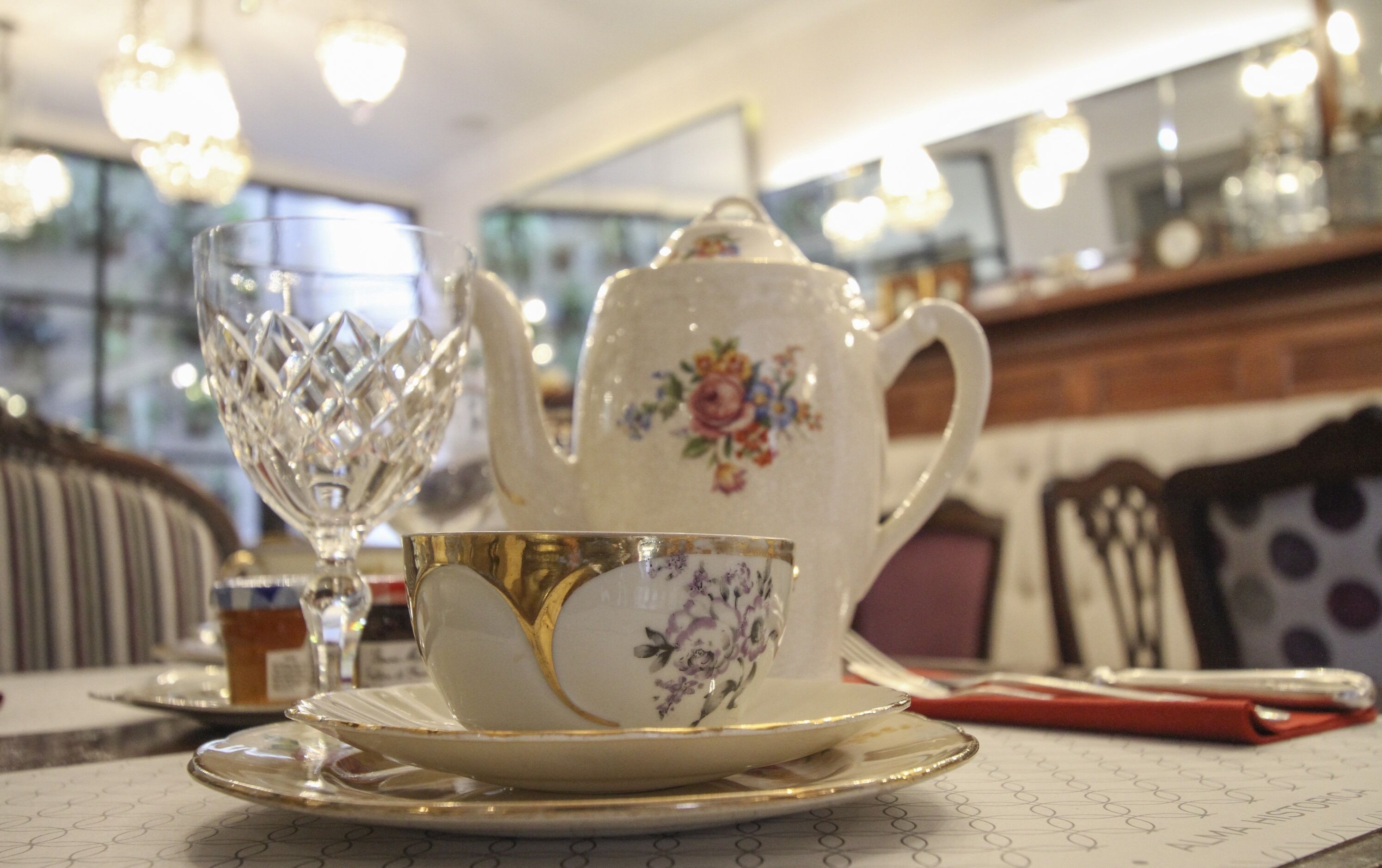 Una mesa dispuesta con tetera, taza y copa de cristal.