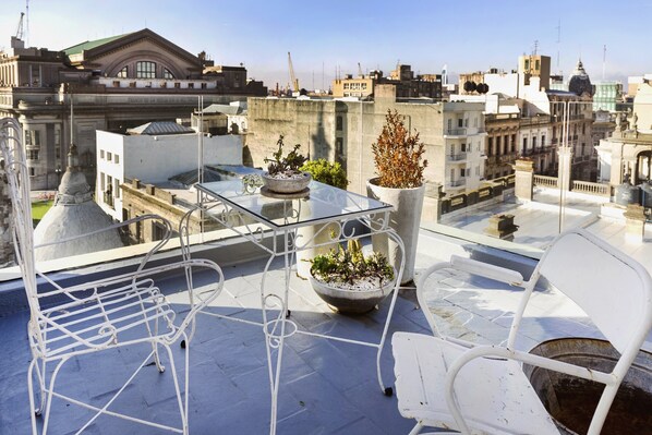 A rooftop terrace with a glass table, two potted plants, and a white metal chair. - Alma Histórica Boutique Hotel (Montevideo)
