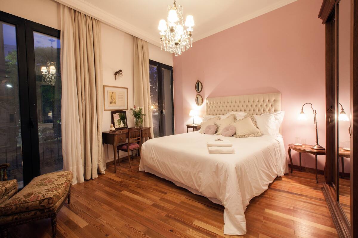 Een slaapkamer met een groot bed, houten vloeren, een kroonluchter en uitzicht door een glazen deur.