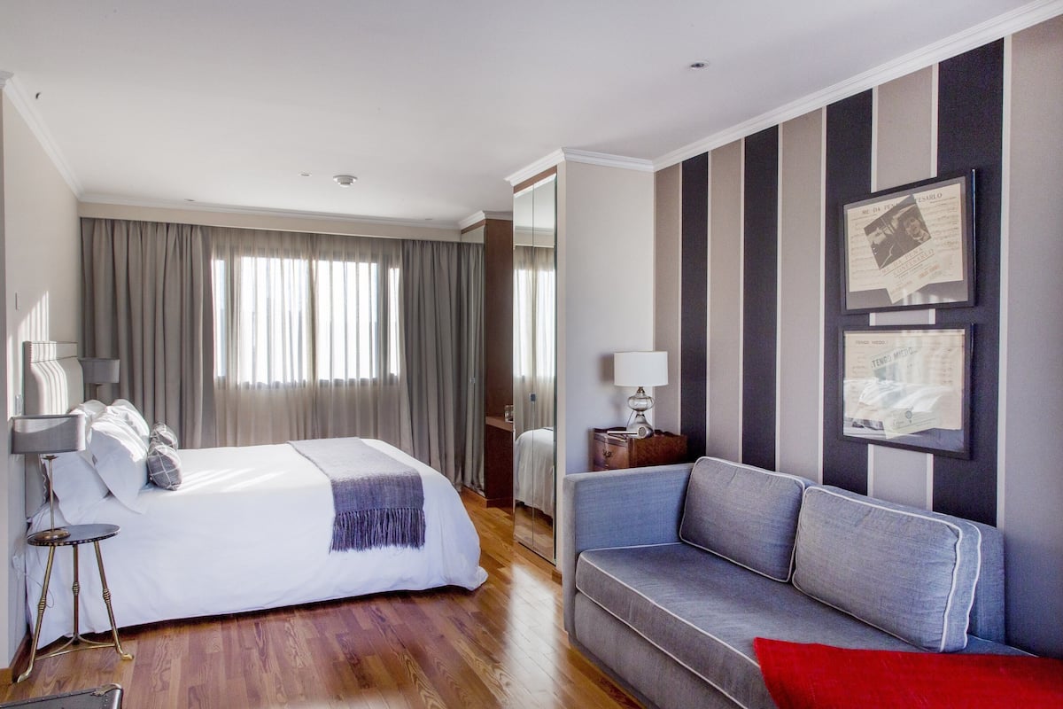 Een hotelkamer met een bed, een bank, een spiegel en lijstjes met foto's aan de muur.
