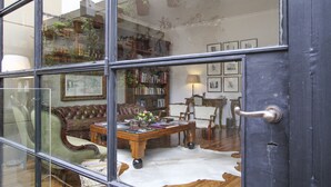 A room with a glass door, a leather sofa, a wooden coffee table with books and a vase, a bookshelf, and a cowhide rug. - Alma Histórica Boutique Hotel (Montevideo)