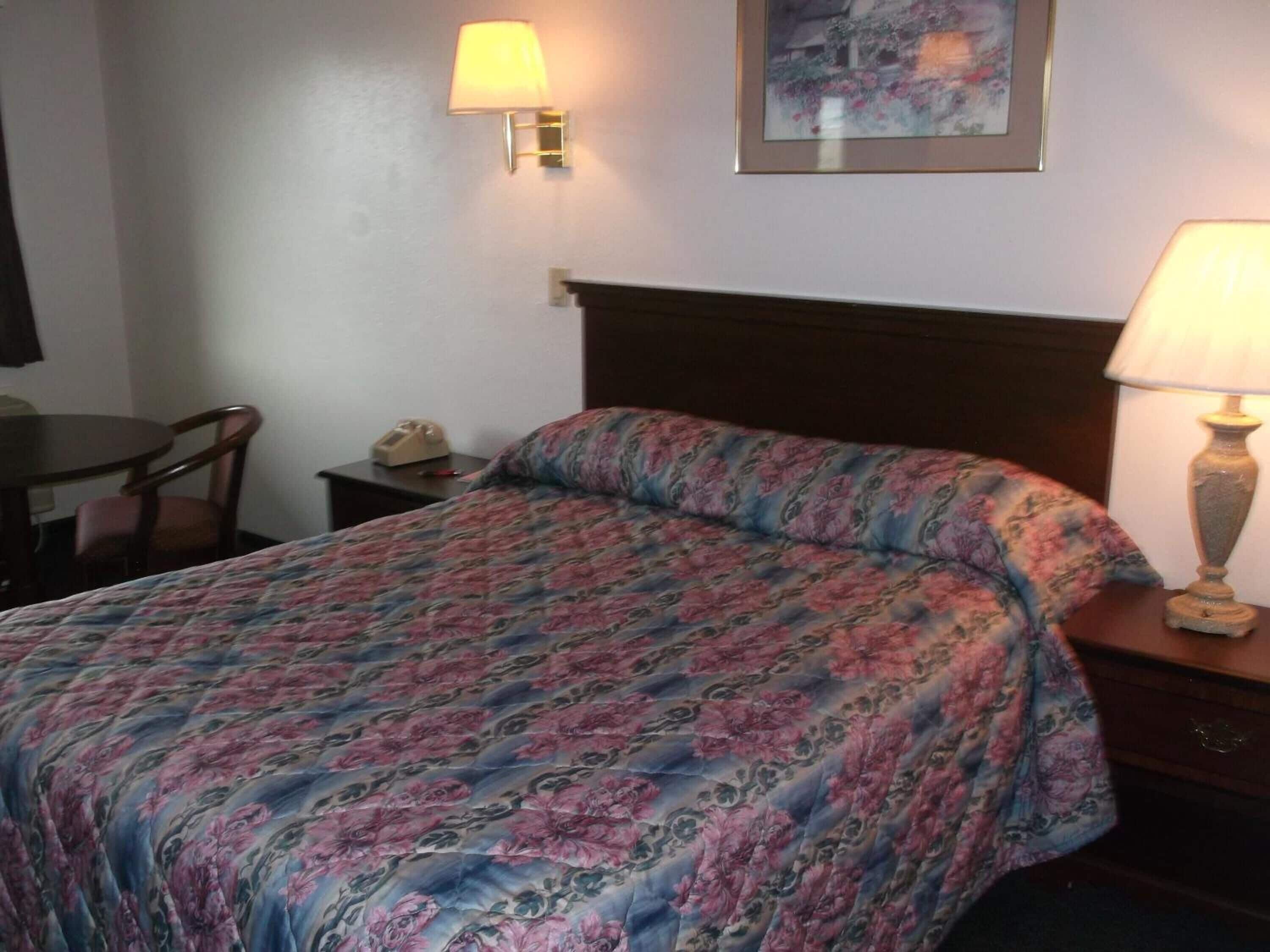 A hotel room with a bed, a nightstand, a desk, and a chair.