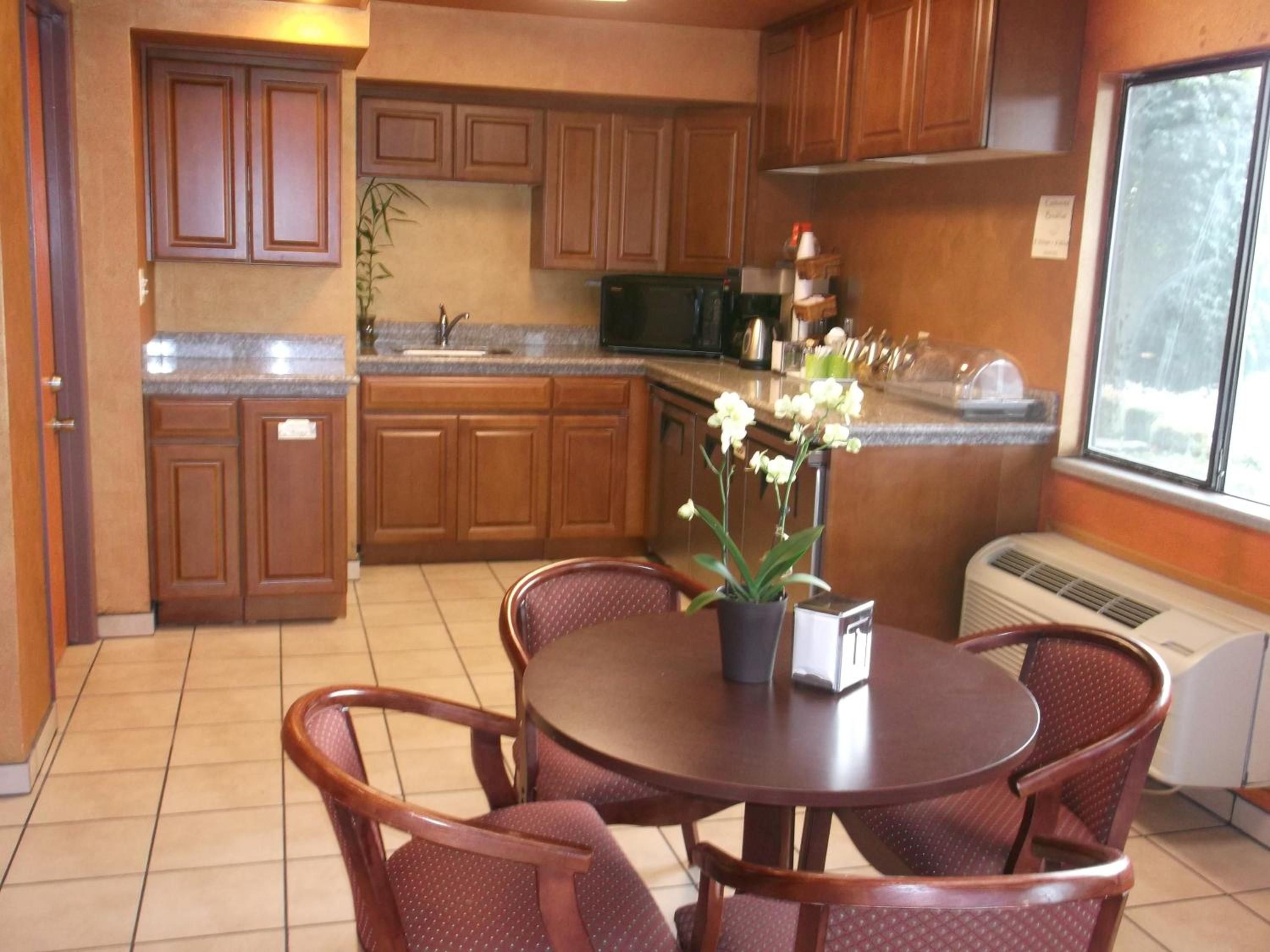 Una cocina con armarios de madera, una mesa de comedor con sillas, una planta en maceta y un ventanal.