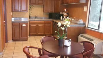 Una cocina con armarios de madera, una mesa de comedor con sillas, una planta en maceta y un ventanal.