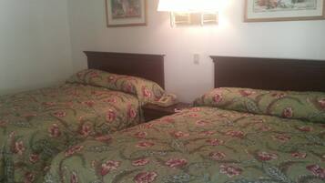 A hotel room with two beds, each with floral bedding, a bedside table with a lamp, and a framed picture on the wall.