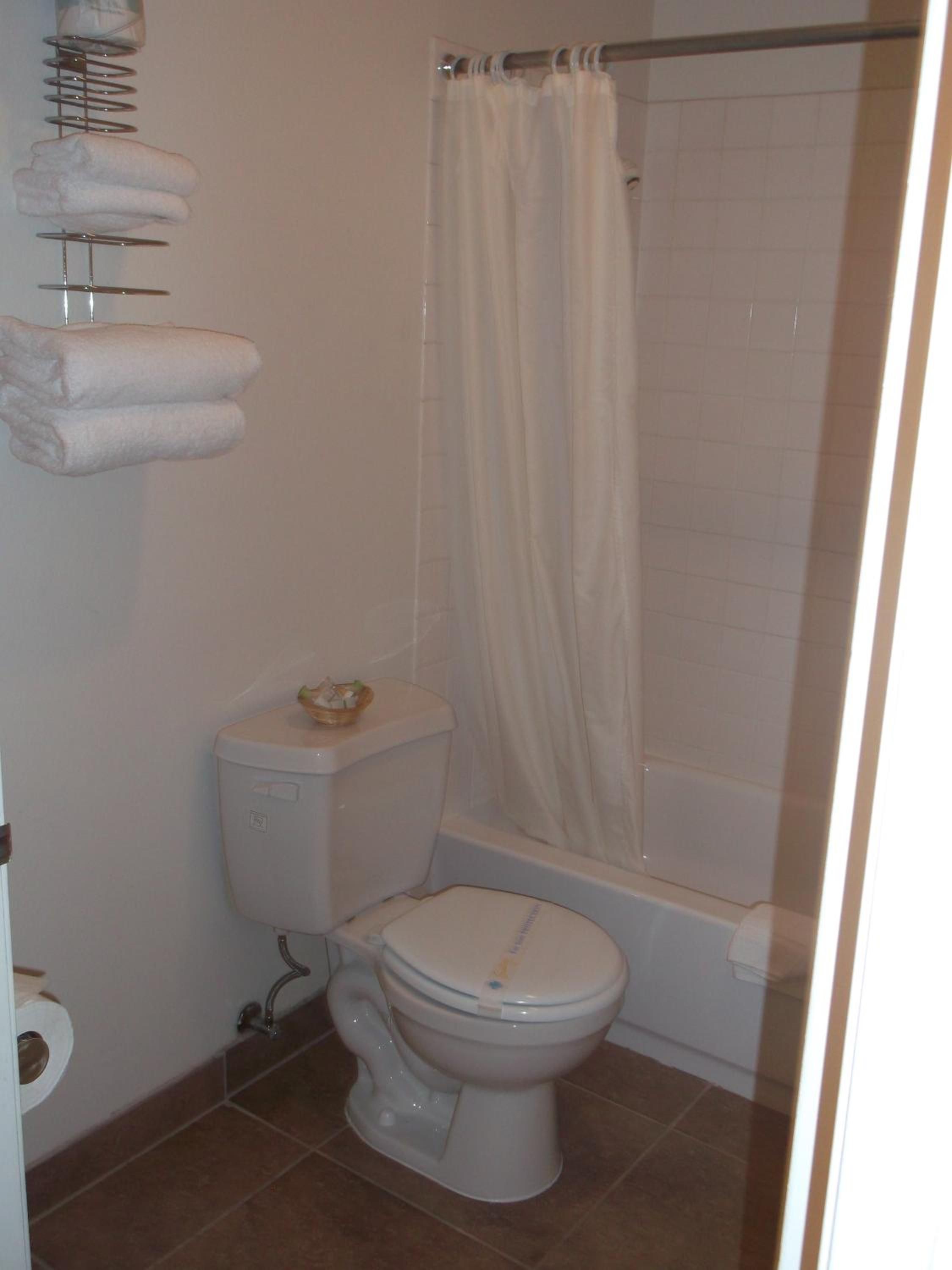 A bathroom with a toilet, a shower with a curtain, and a towel rack with folded towels.