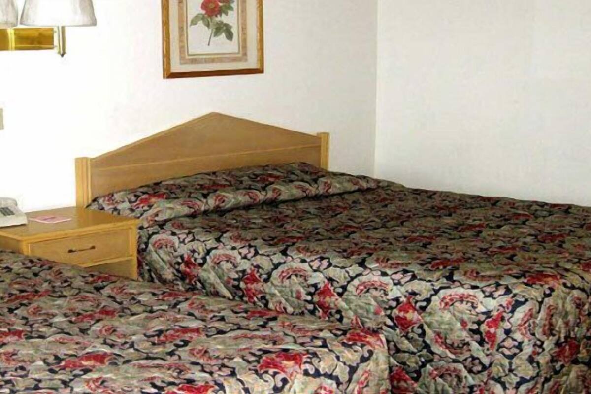 A room with two single beds, each with floral-patterned bedding. There is a bedside table with a lamp and a telephone.