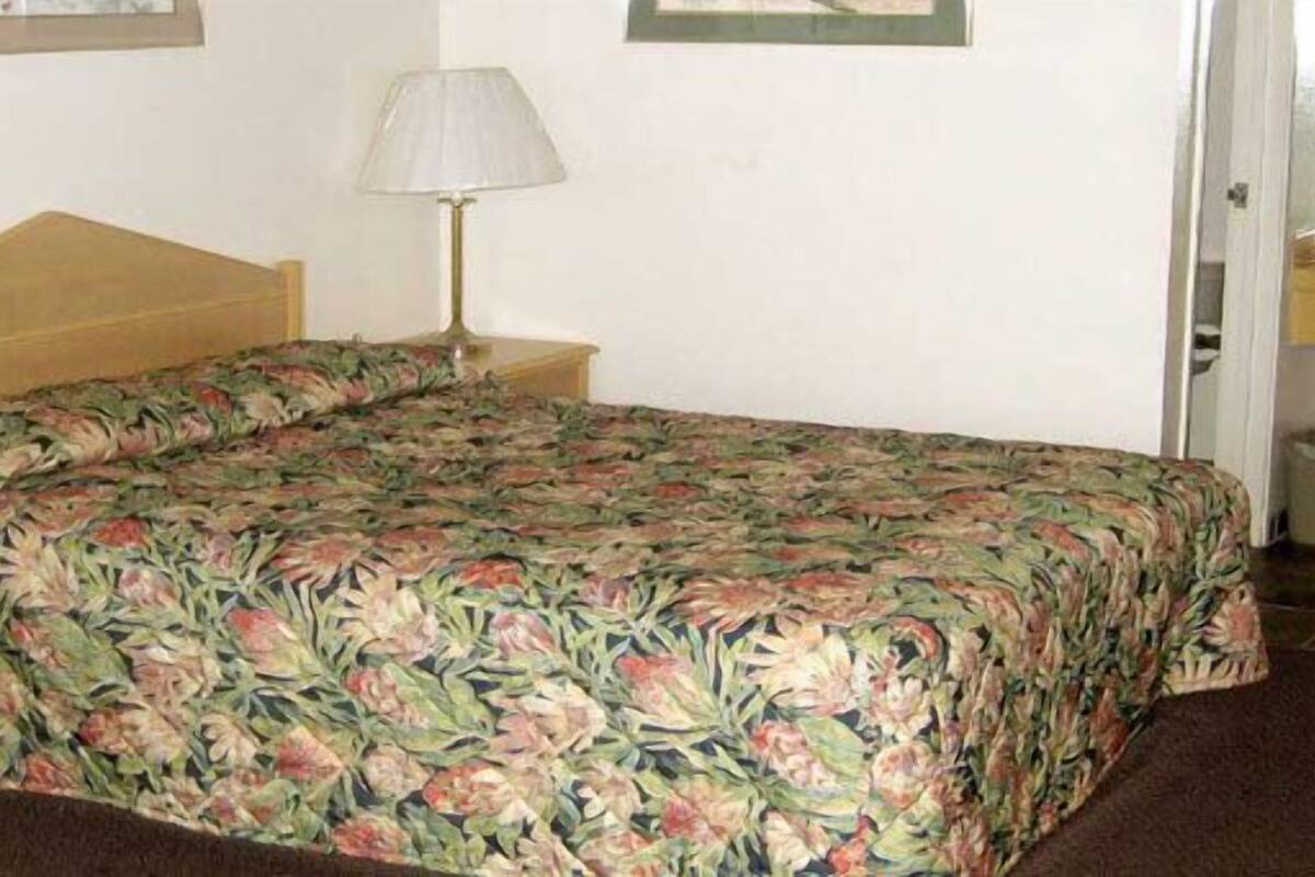 A hotel room with a floral bedspread, a bedside lamp, a telephone, and a bathroom with a sink and mirror.