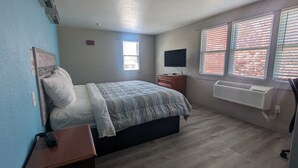 A bedroom with a bed, a dresser, a TV, a window with blinds, and an air conditioner. - Hyannis Host Inn (Hyannis)