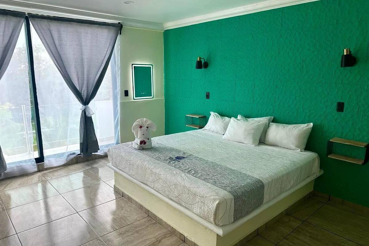 Un dormitorio con cama, cortinas, una mesita pequeña y una lámpara de pared.