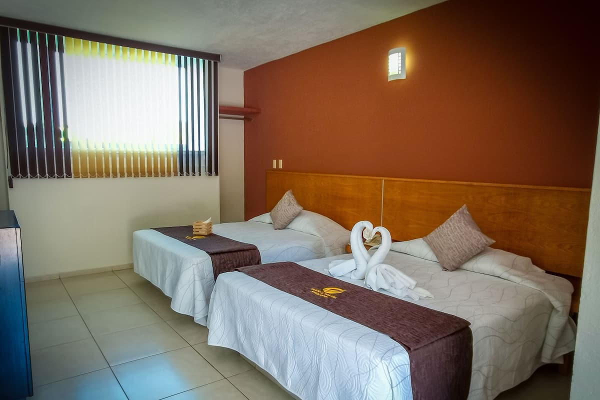 Habitación de hotel con dos camas, cabecera de madera, mesita de noche y ventana con persianas.