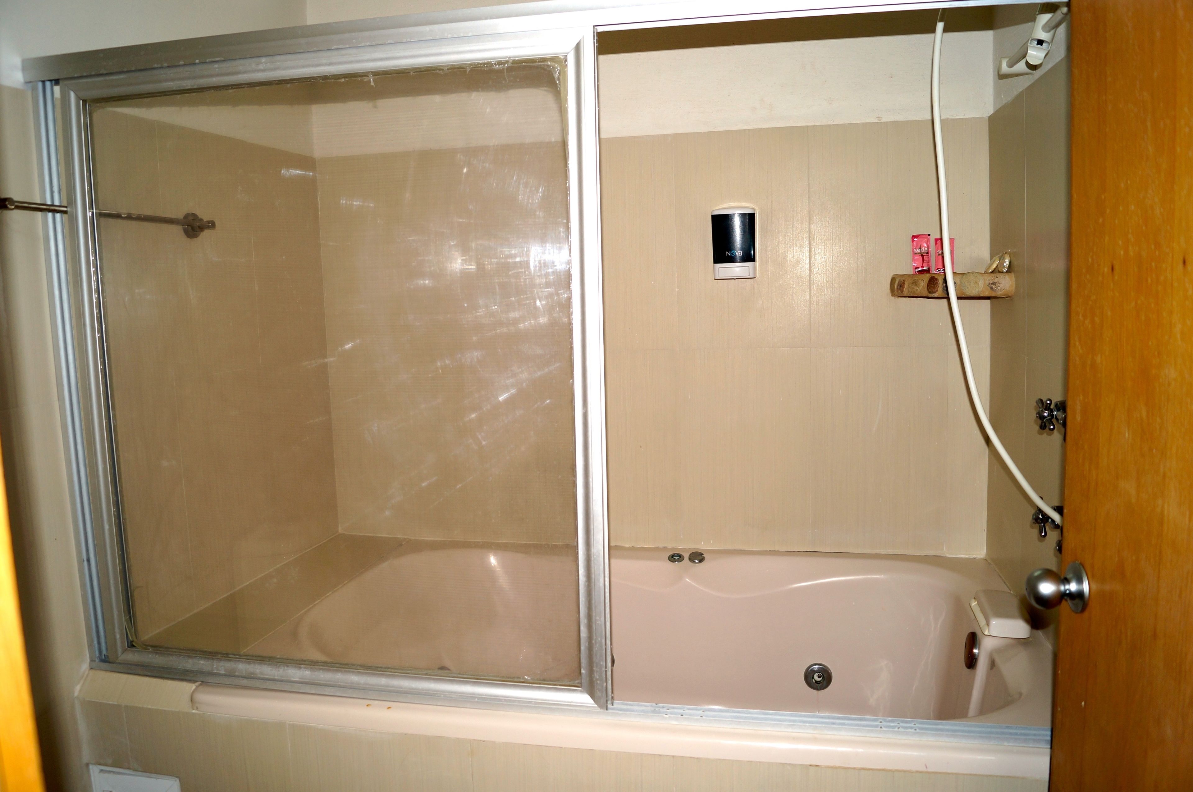 Een badkamer met een douchecabine van glas, een bad en een houten plankje met toiletartikelen.