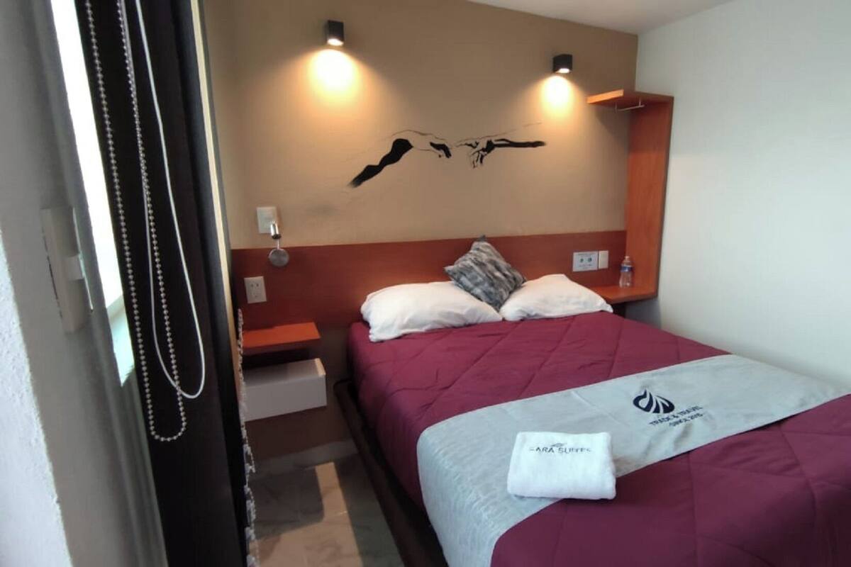 Habitación de hotel con cama, mesita de noche, lámpara de pared y una toalla sobre la cama.