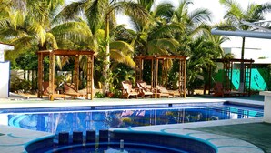 A swimming pool with a wooden deck and lounge chairs, surrounded by palm trees. - Sara Suites Ixtapa (Ixtapa)