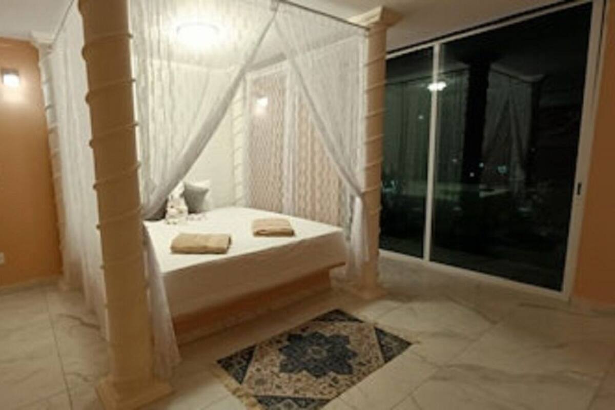 Un dormitorio con cama con dosel, puerta corrediza de vidrio y alfombra estampada.