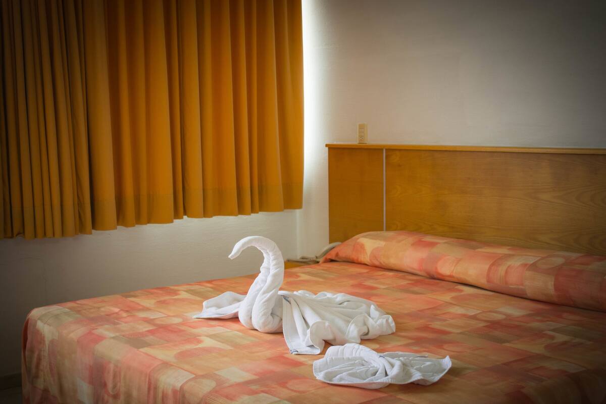Una habitación de hotel con una cama, cabecera de madera y una ventana con cortinas.