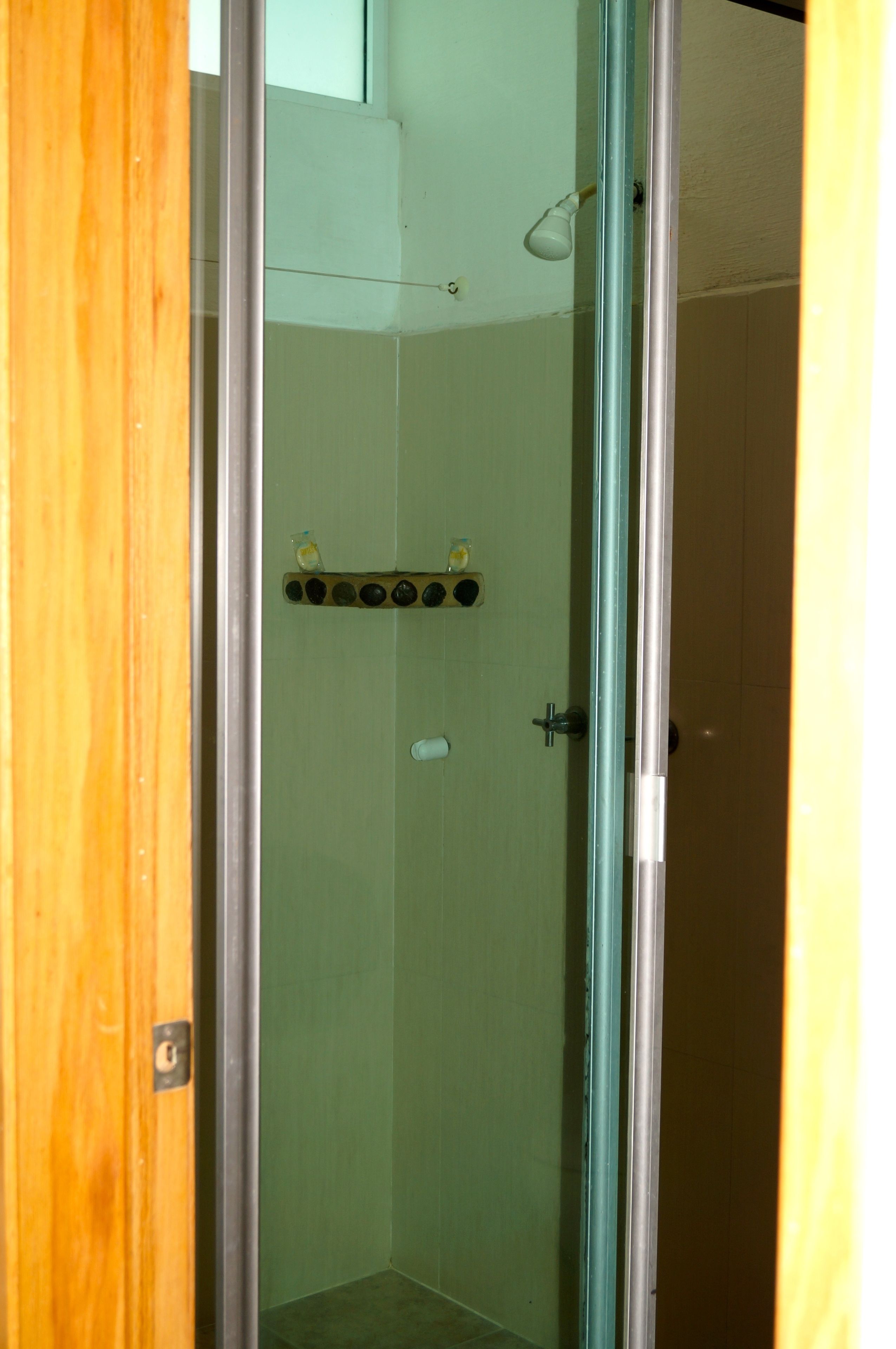 Un box de ducha con paredes y puerta de cristal, un cabezal de ducha y un jabonera en la pared.
