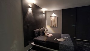 A modern hotel room with a bed, pillows, a small table, and a framed picture on the wall. - Sara Suites Ixtapa (Ixtapa)