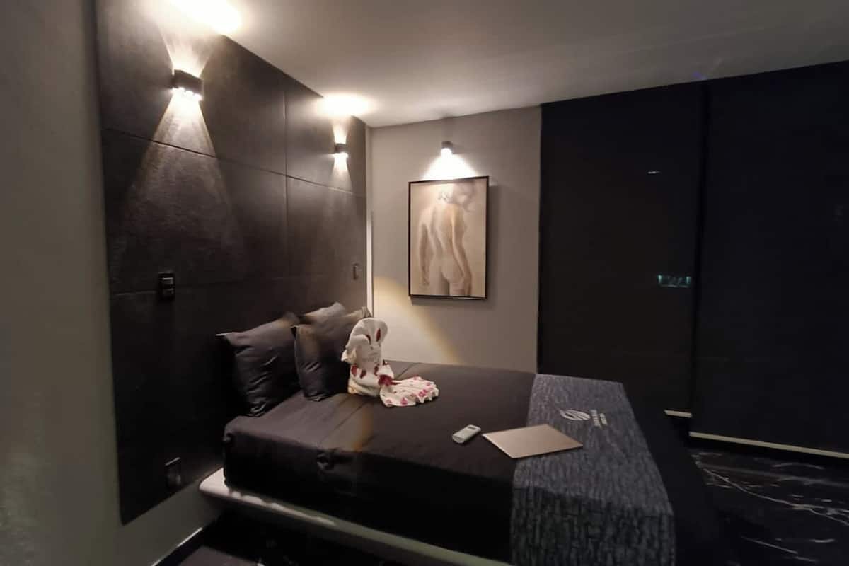 Una habitación de hotel moderna con una cama, almohadas, una mesita y un cuadro en la pared.