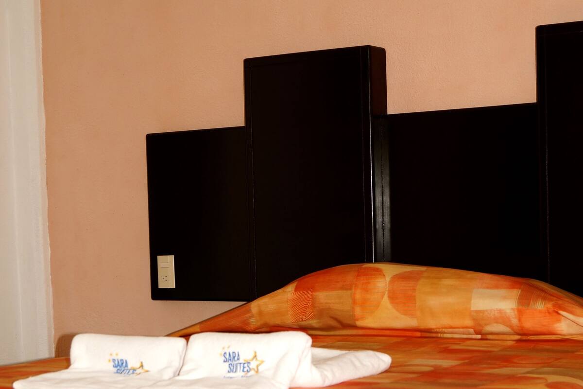 Una habitación de hotel con una cama, un cabecero y un televisor instalado en la pared.