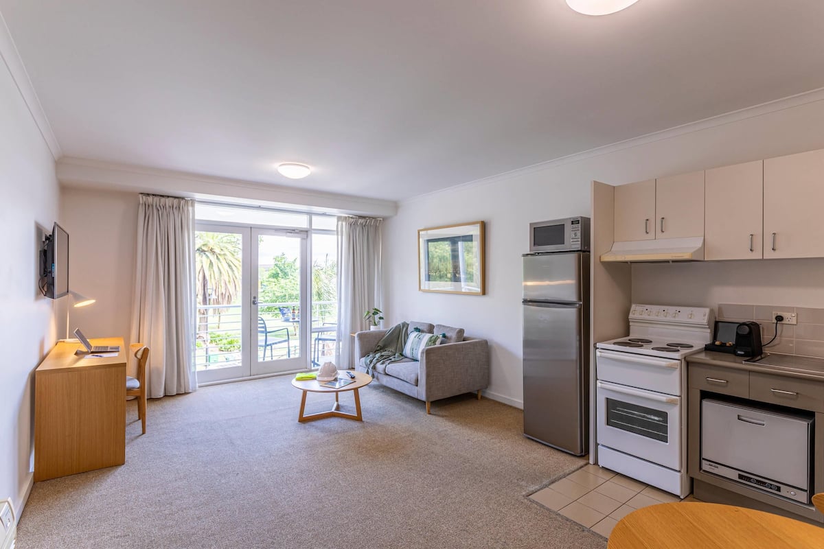 A modern kitchen with a refrigerator, stove, and microwave. There is a dining table and a sofa in the living area.