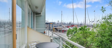 A balcony with a table and chairs, overlooking a marina with boats and a city skyline.