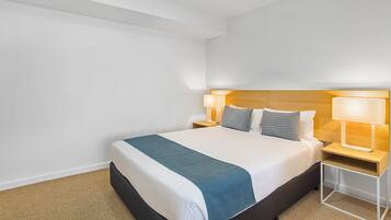 Una habitación de hotel con una cama grande, dos mesitas de noche con lámparas y un cabecero de madera.