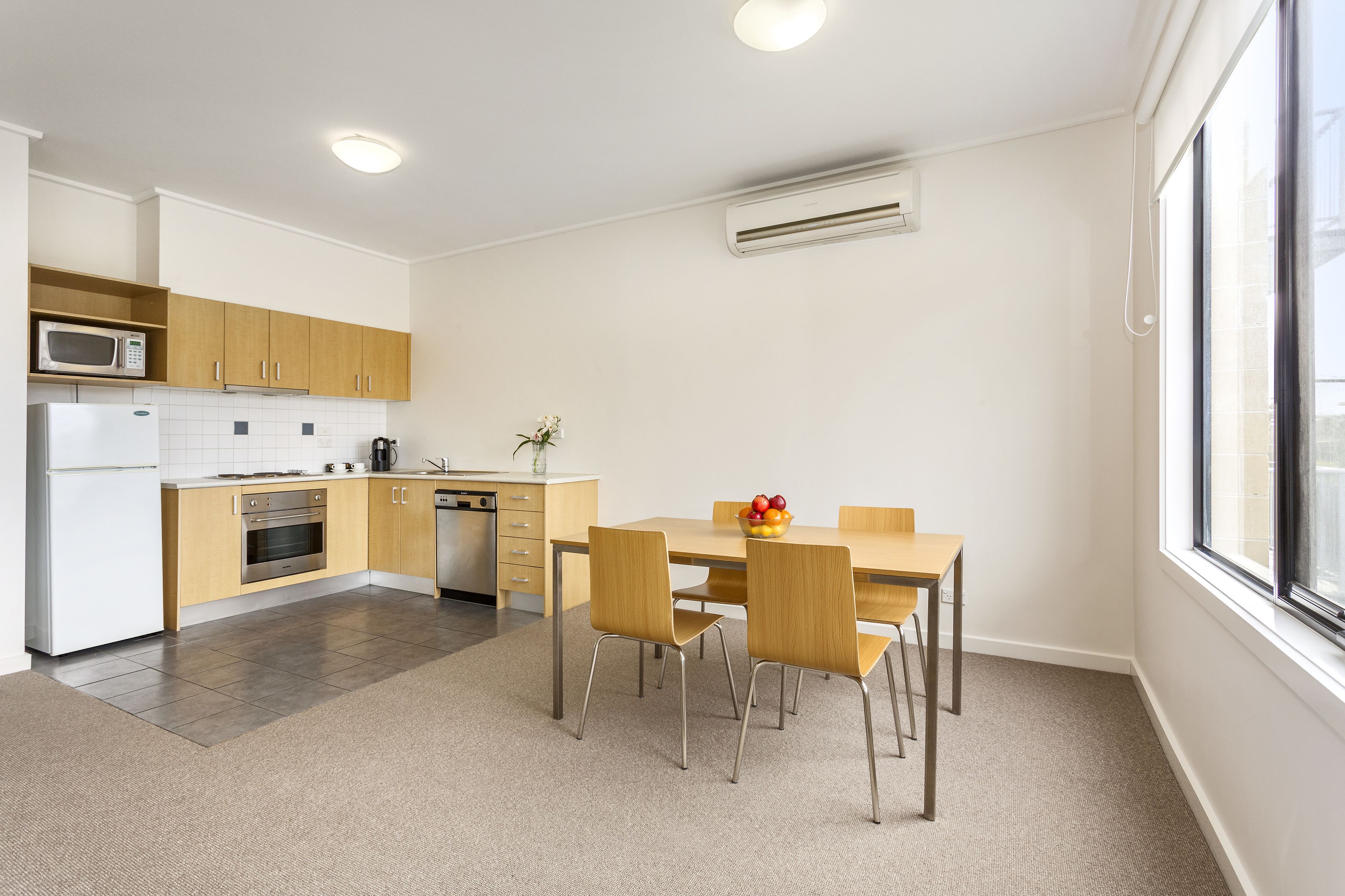 Una cocina moderna con armarios de madera, un refrigerador blanco y un comedor con mesa y sillas.