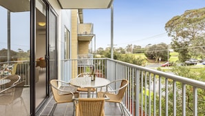A balcony with a glass door, wicker chairs, a round table, and a bottle of wine. - Quest Frankston (Frankston)